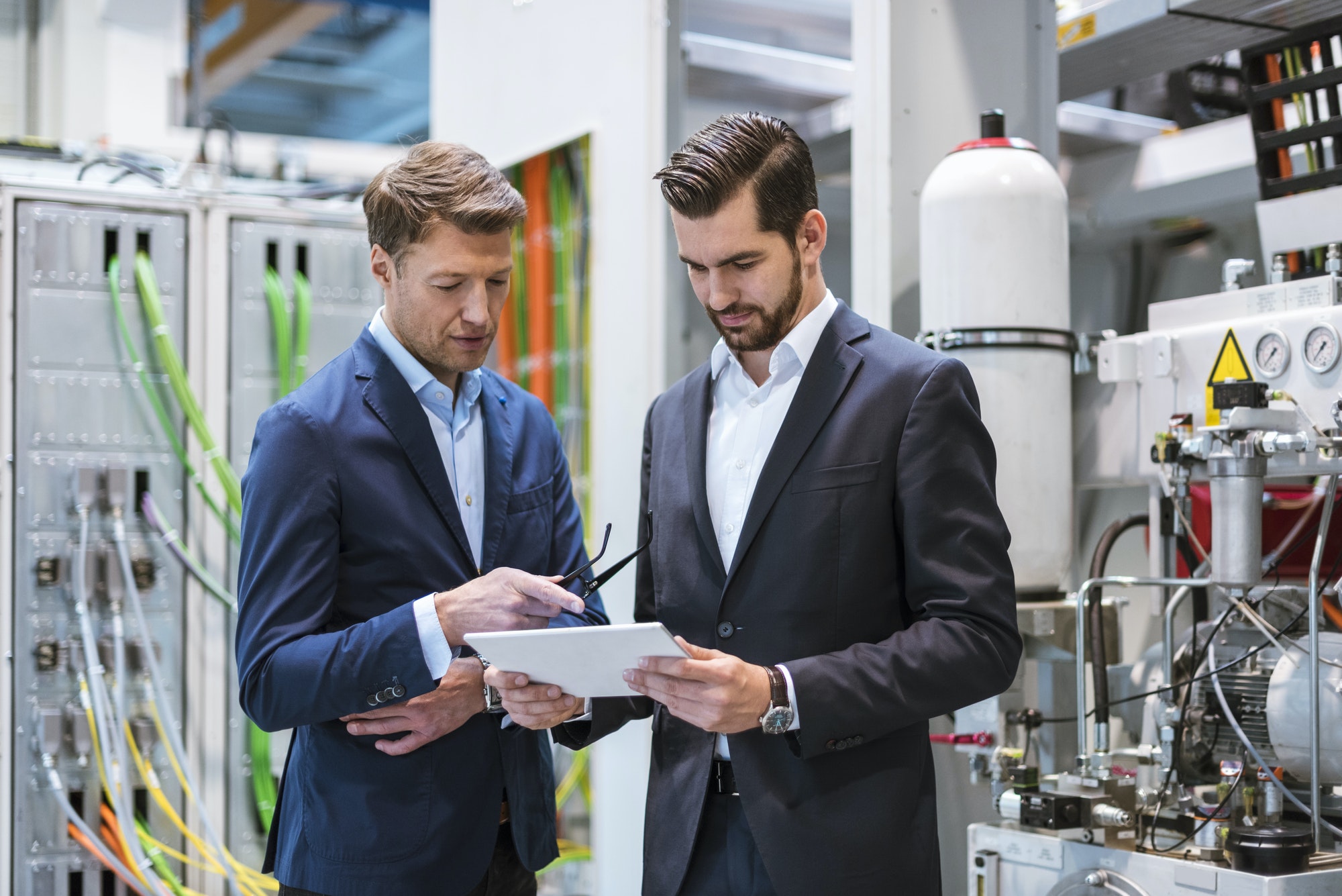 Two businessmen in factory looking at tablet